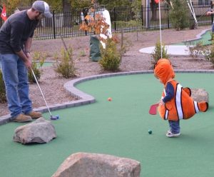 costumed boy plays mini golf with his dad